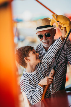 Grandfather And Grandson Having Fun And Spending Good Quality Time Together In Amusement Park. Kid Shooting With Air Gun While Grandpa Helps Him To Win The Prize.