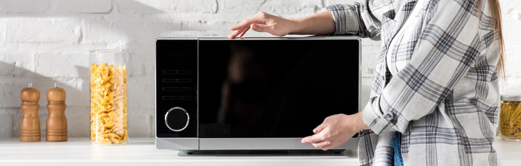 panoramic shot of woman in shirt touching microwave in kitchen