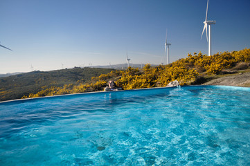 Obraz premium Blue water in the pool in the background wind farm behind the field yellow bushes . The Flintstone House Portugal