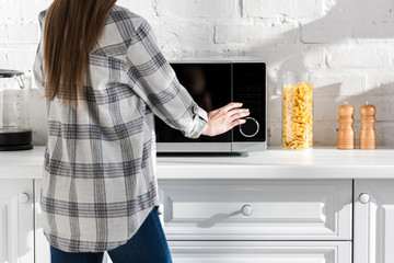 cropped view of woman in shirt using microwave in kitchen - obrazy, fototapety, plakaty