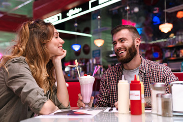 Loving couple sit in retro bright cafe drinking cockail indoors.