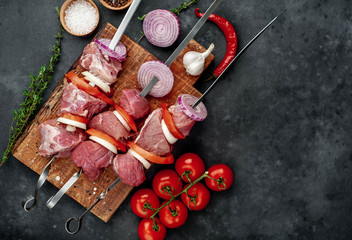 Raw skewers of meat. Barbecue meat with vegetables and spices on a stone background. 