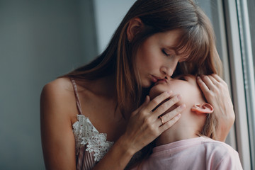 Mother hug and kiss with a little daughter at window. Close up portrait,