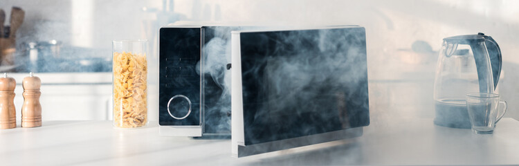 panoramic shot of broken and steamy microwave on table in kitchen