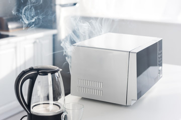 electric kettle, broken and steamy microwave on table in kitchen