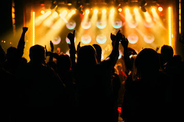 Fototapeta na wymiar Crowd at a music concert, audience raising hands up in front of bright stage lights.