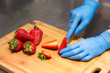 hands in blue gloves cut red strawberries on a wooden Board for fruit salad.