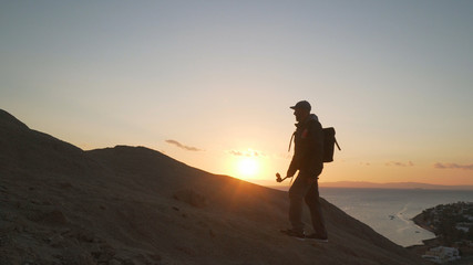 Handsome senior traveler with selfie stick climb up a hill at sunrise