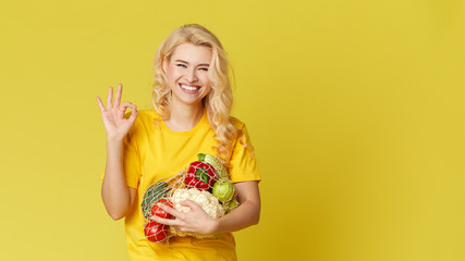 Young woman hold a string bag full of organic vegetables on yellow background. Happy face. Emty space for text. Healthy Eating, Vegetarianism