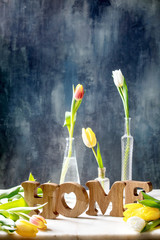 Wooden decorative letters word HOME with colorful tulips on white marble table with dark blue wall behind. Spring home decoration.