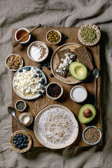Fototapeta na wymiar Healthy breakfast. Variety of breakfast dishes wheat, yogurt, kefir, cottage cheese, avocado, rye bread, seeds, nuts and berries assortment in ceramic bowls. Wooden and textile background. Flat lay