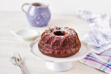 Chocolate bundt cake with icing sugar on wooden table, rustic style