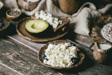 Healthy breakfast. Variety of breakfast dishes sprouted wheat, yogurt, kefir, cottage cheese, avocado, rye bread, seeds, nuts and berries assortment in ceramic bowls over rustic wooden table.