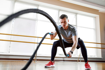 Athletic man doing rope exercise. Sneaker with ropes in the sports concept of the gym.