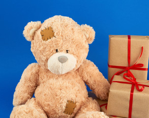 cute big beige teddy bear holds a brown box with a red ribbon