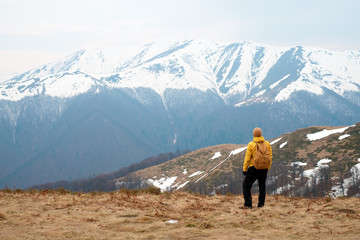 Naklejka na ściany i meble Man in yellow jacket with backpack in spring snowy mountains. Travel concept. Landscape photography