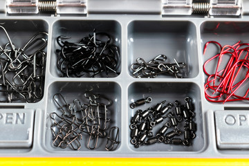 Opened tackle box with fishing hooks and accessories. Fishing hooks in box sections. Case for tackle elements. Fishing accessories background close-up.