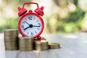 Fotobehang A red alarm clock and a pile of coins resting on the table. Ideas to save money, ideas for business growth, use the right time to invest, the idea of using time to be worth the money. Investment risk. © Kanjana