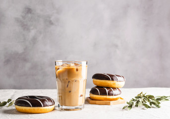Iced coffee and chocolate donuts on the table against gray background. Refreshing coffee drink...