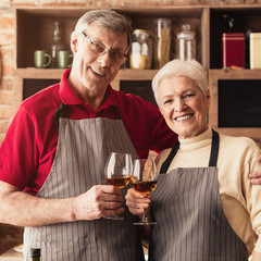 Happy senior beloved man and woman enjoying wine at kitchen