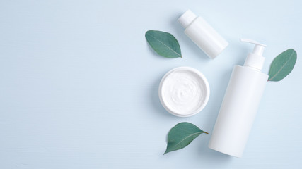 Natural organic cosmetic bottle container, body cream, essential oil and green leaves. SPA cosmetic products branding mockup. Minimalist flat lay style