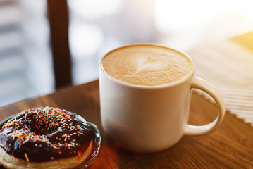 Coffee with a drawn heart and milk on a wooden table in a coffee shop. Chocolate donut with...