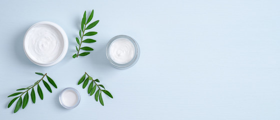 Jars of organic cosmetic cream and green leaves on blue background. Organic natural cosmetic...