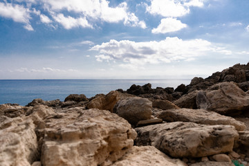 Mediterranean Sea in Northern Cyprus. Summer rocky coast, transparent calm blue water and white clouds on blue sky. Seascape.