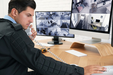 Male security guard talking by telephone near monitors at workplace