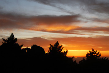 Huangshan Mountain in Anhui Province, China. Sunset over Huangshan with colorful sky and clouds and a silhouette of the trees. Sun nearly set. Sunset near the summit of Huangshan Mountain, China.