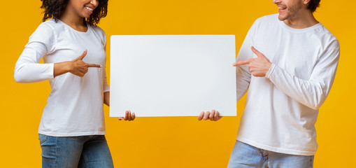 Interracial Couple Pointing At White Advertisement Placard In Their Hands