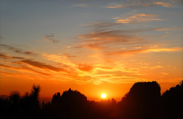 Huangshan Mountain in Anhui Province, China. Sunrise over Huangshan with colorful sky and clouds. Horizon in focus. Foreground trees not in focus. Sunrise near the summit of Huangshan Mountain, China.