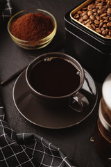 Obraz na płótnie Canvas A black coffee Cup,a checkered towel, a metal jar of roasted coffee beans on a dark concrete table