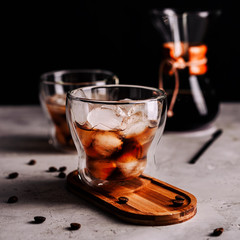 Iced coffee in a glass with ice cubes on wooden tray,scattered grains on concrete background