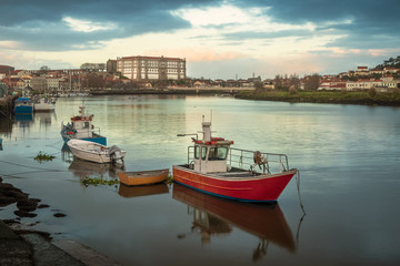 Fototapeta na wymiar View of the Ave river in Vila do Conde, Portugal, with fishing boats anchored in the foreground and the Santa Clara convent in the background, at the end of an autumn day.