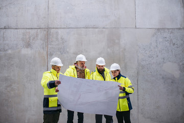 A group of engineers standing against concrete wall on construction site.