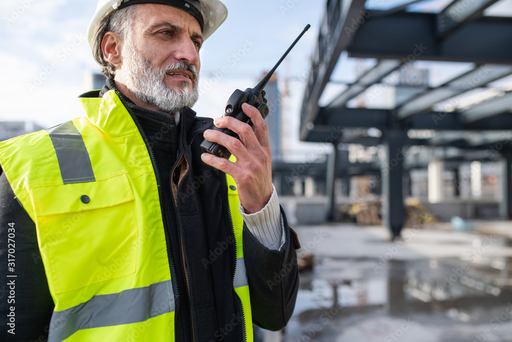 Wall mural Man engineer using walkie talkie on construction site.