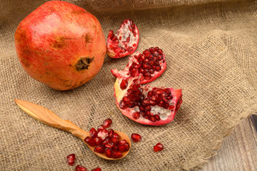 Ripe juicy pomegranate, pieces of pomegranate and pomegranate seeds on a wooden spoon on a...