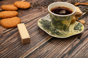 A Cup of black tea, tea leaves, pieces of brown sugar, oatmeal cookies, waffles on a wooden background. Close up.
