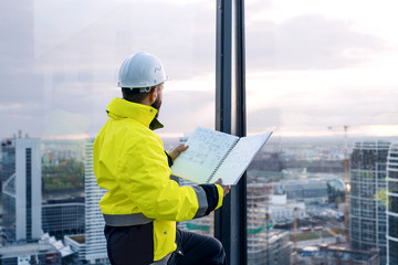 Man engineer standing on construction site, holding blueprints.