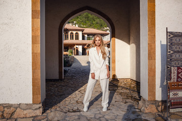 Fototapeta na wymiar Outdoor full body fashion portrait of fashionable woman in white suit posing in street of east city