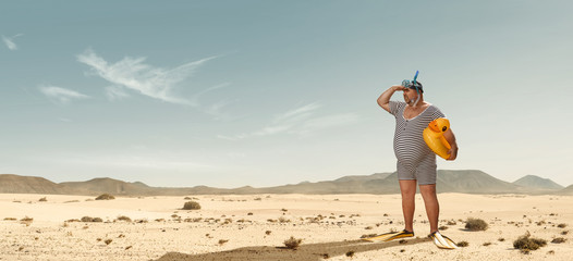 Funny overweight swimmer looking for the beach  in the middle of the desert with copy space - obrazy, fototapety, plakaty