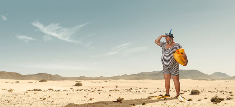 Funny overweight swimmer looking for the beach  in the middle of the desert with copy space