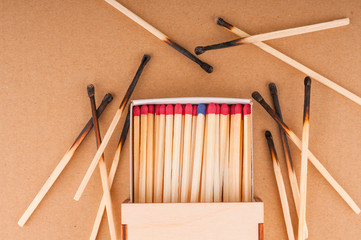 Matchbox full of matches and burnt matches on brown background