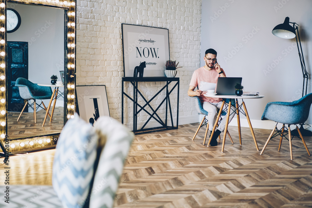 Aufkleber young man talking via smartphone app while working remotely on modern netbook with wireless internet