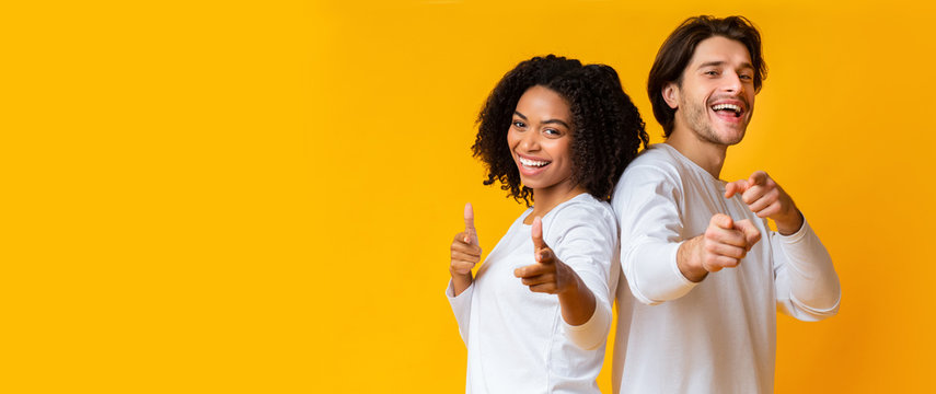 Cheerful interracial couple pointing at camera and laughing