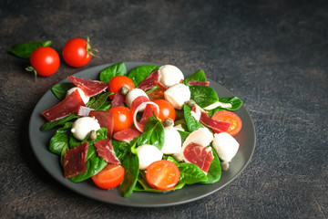 Salad with prosciutto, mozzarella, fresh vegetables on a dark plate on a black background.