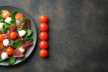 Salad with prosciutto, mozzarella, fresh vegetables on a dark plate on a black background top view copy space.