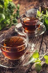 A cup of melissa tea with herbs on wooden table