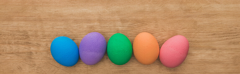 top view of rainbow painted Easter eggs on wooden table, panoramic shot